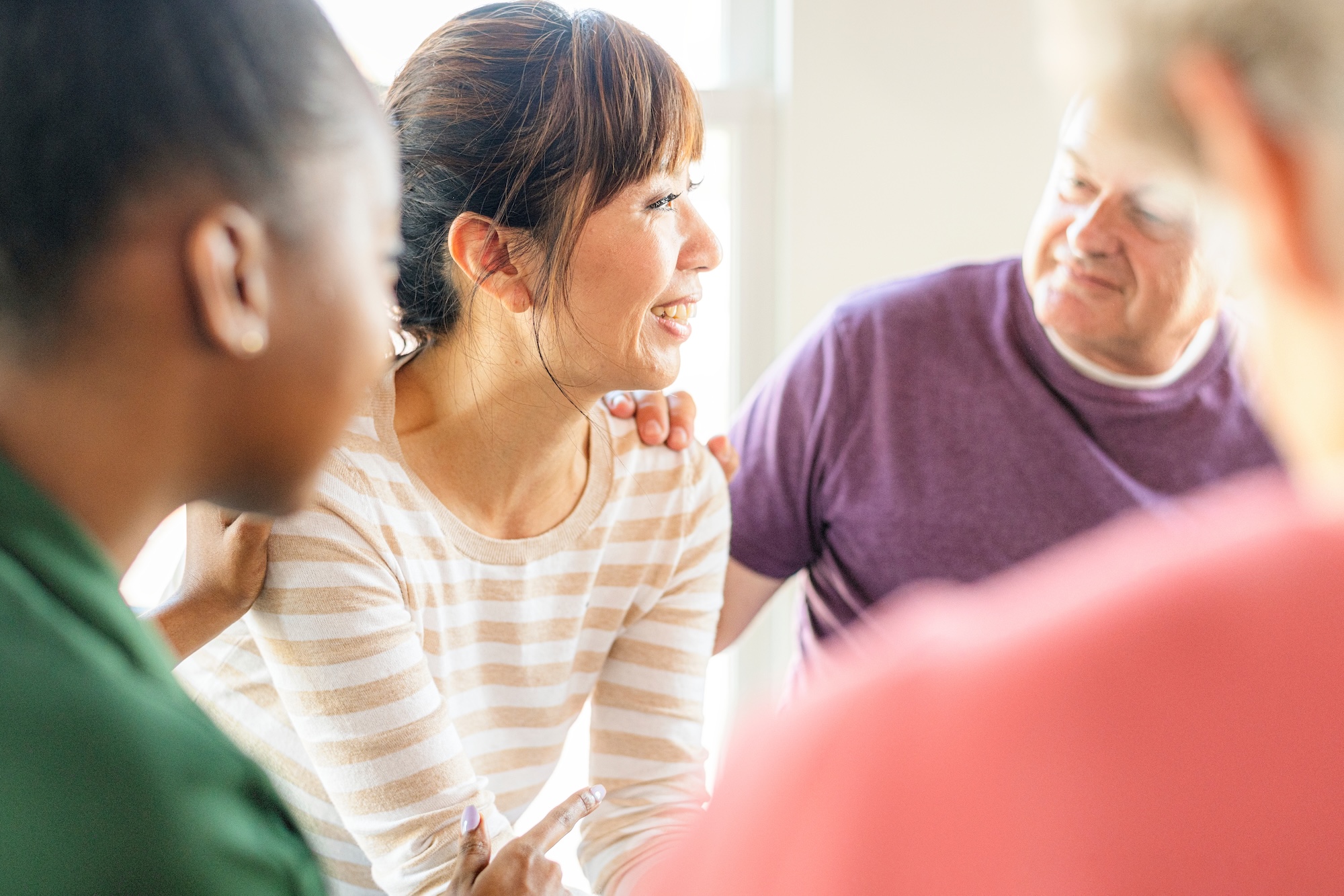 Group counseling session with diverse participants engaging in supportive conversation, emphasizing connection and emotional support in a therapeutic setting.